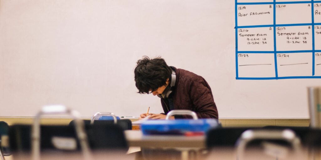 Ein Student sitzt allein in einem Raum und schreibt handschriftlich